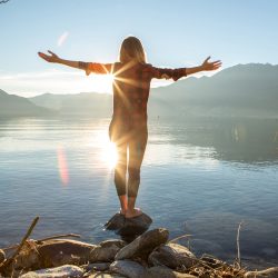 Young cheerful woman by the lake enjoying nature. Arms outstretched for positive emotion.